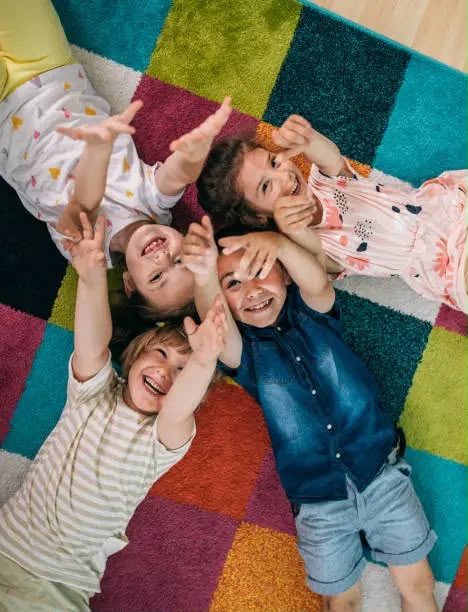Kinder liegen lachend im Kreis auf einem bunten Teppich